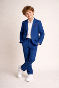 Young boy wearing a blue suit with a white shirt and white sneakers on a beige background