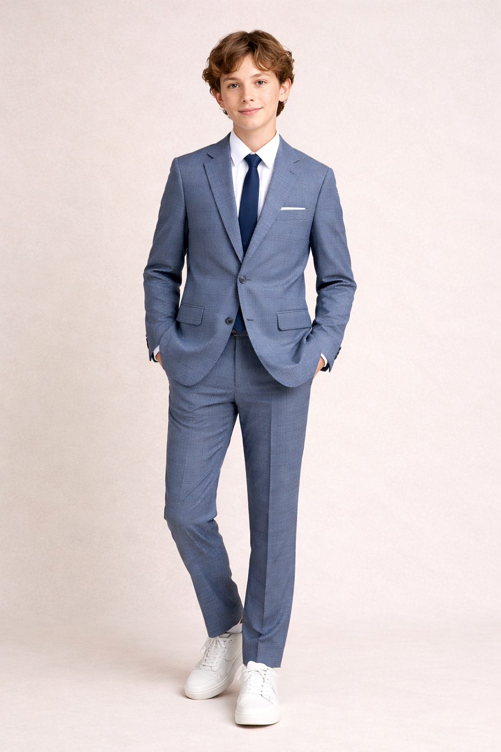 Young boy wearing a blue suit with a white shirt and white shoes on a beige background