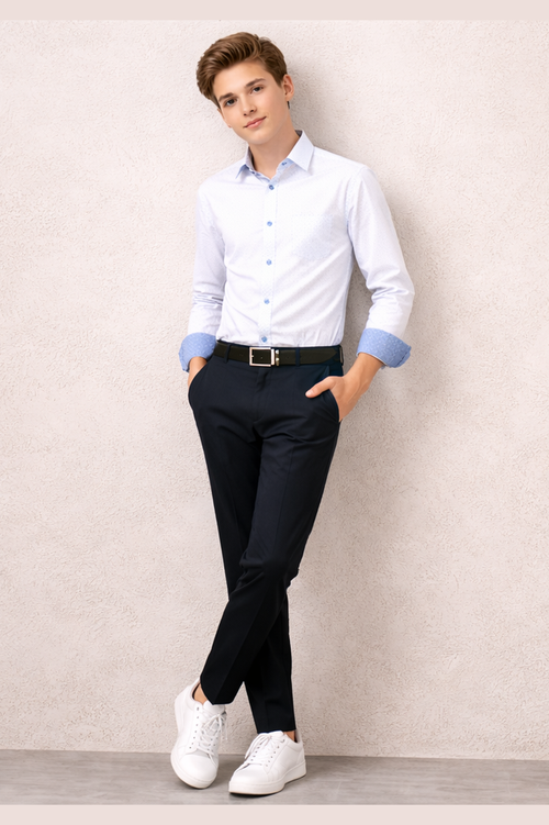 Boy wearing a white dress shirt with rolled-up sleeves, black pants, and white sneakers against a plain wall.